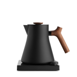 Matte black electric kettle with angled wooden handle and lid knob on a square base.