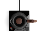 Matte black electric kettle with wooden handle and base on a glossy black induction plate with digital display.