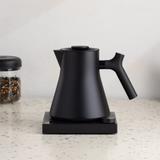 Matte black electric kettle with angled handle and gooseneck spout on square base.