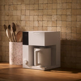 Compact white coffee maker with a modern rectangular design and integrated cup on a wooden countertop.