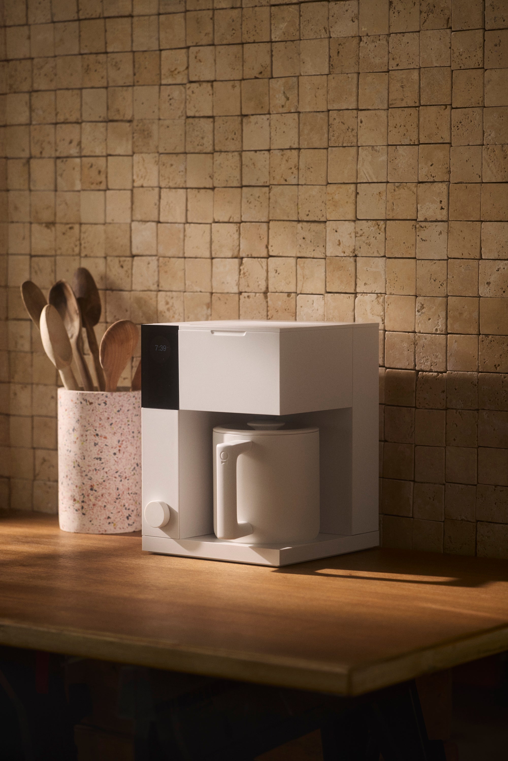 Compact white coffee maker with a modern rectangular design and integrated cup on a wooden countertop.
