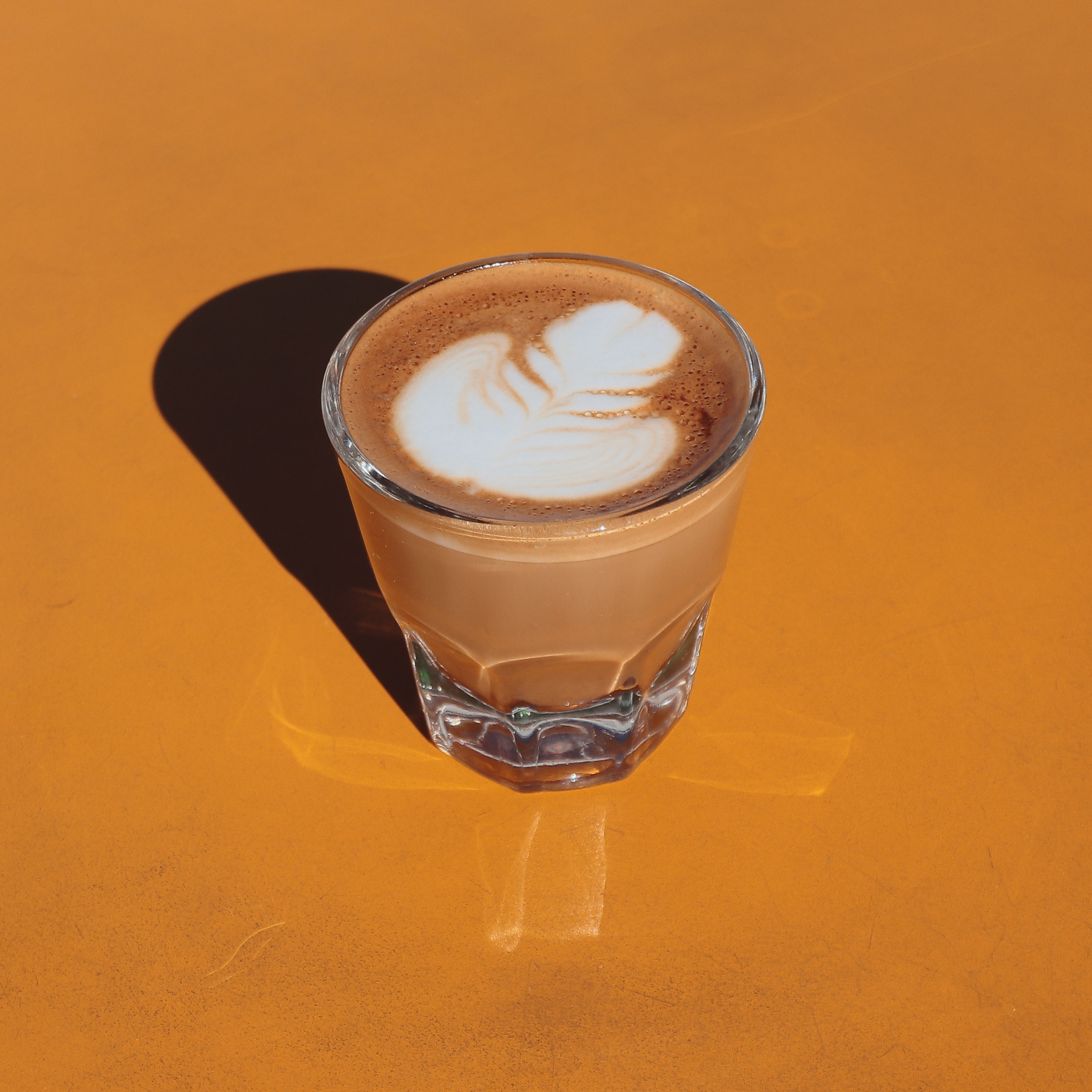 Glass of cappuccino with latte art on an orange surface