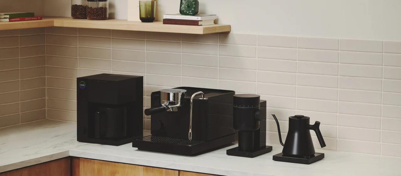 Black coffee maker and kettle on a kitchen counter with tiled wall in the background