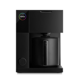 Matte black precision coffee maker with cylindrical carafe and digital touchscreen display on top left.