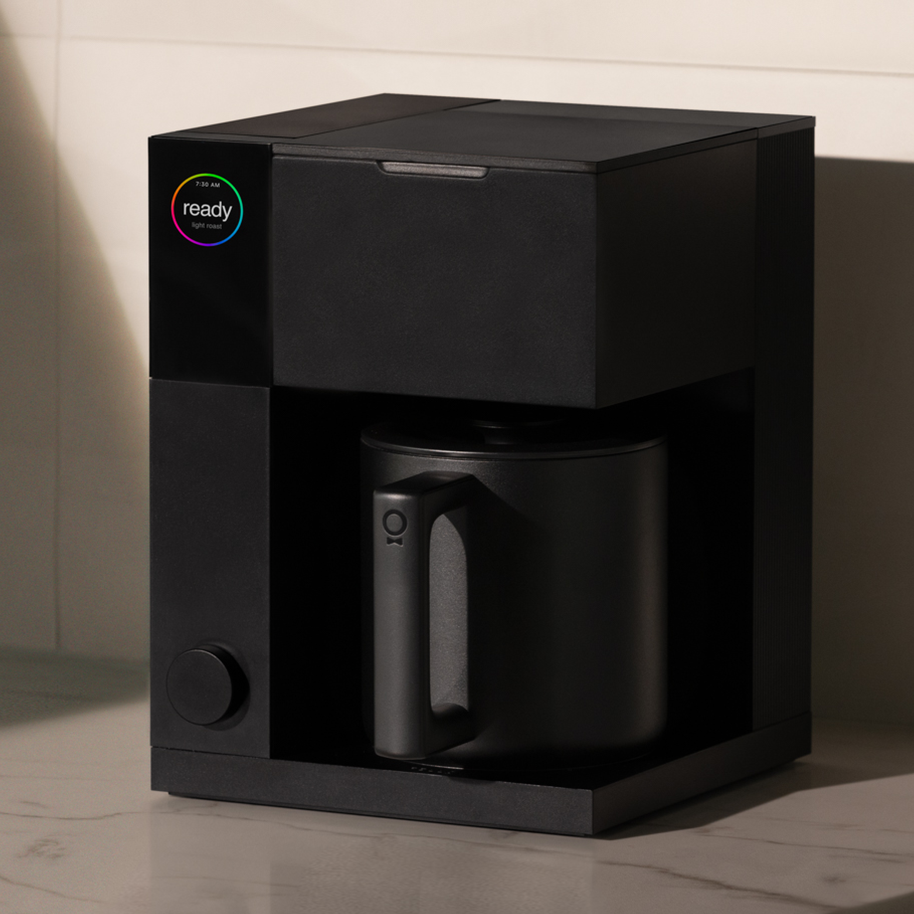 Compact matte black precision coffee maker with a cylindrical carafe and minimalist control knob.