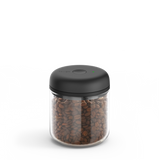 Clear cylindrical glass canister with a matte black lid and filled with coffee beans.