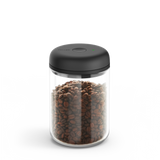 Clear cylindrical glass canister with black electric vacuum-sealed lid filled with coffee beans.