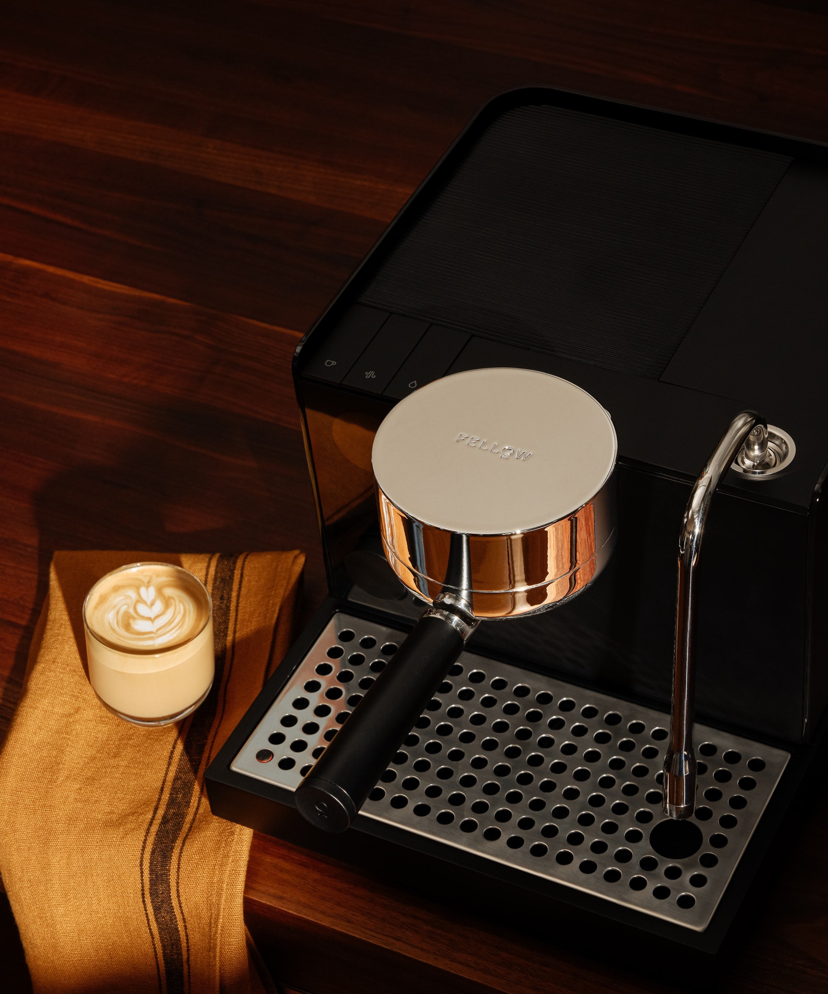 Matte black espresso machine with silver accents, steam wand, and drip tray on wooden surface with latte and cloth nearby.