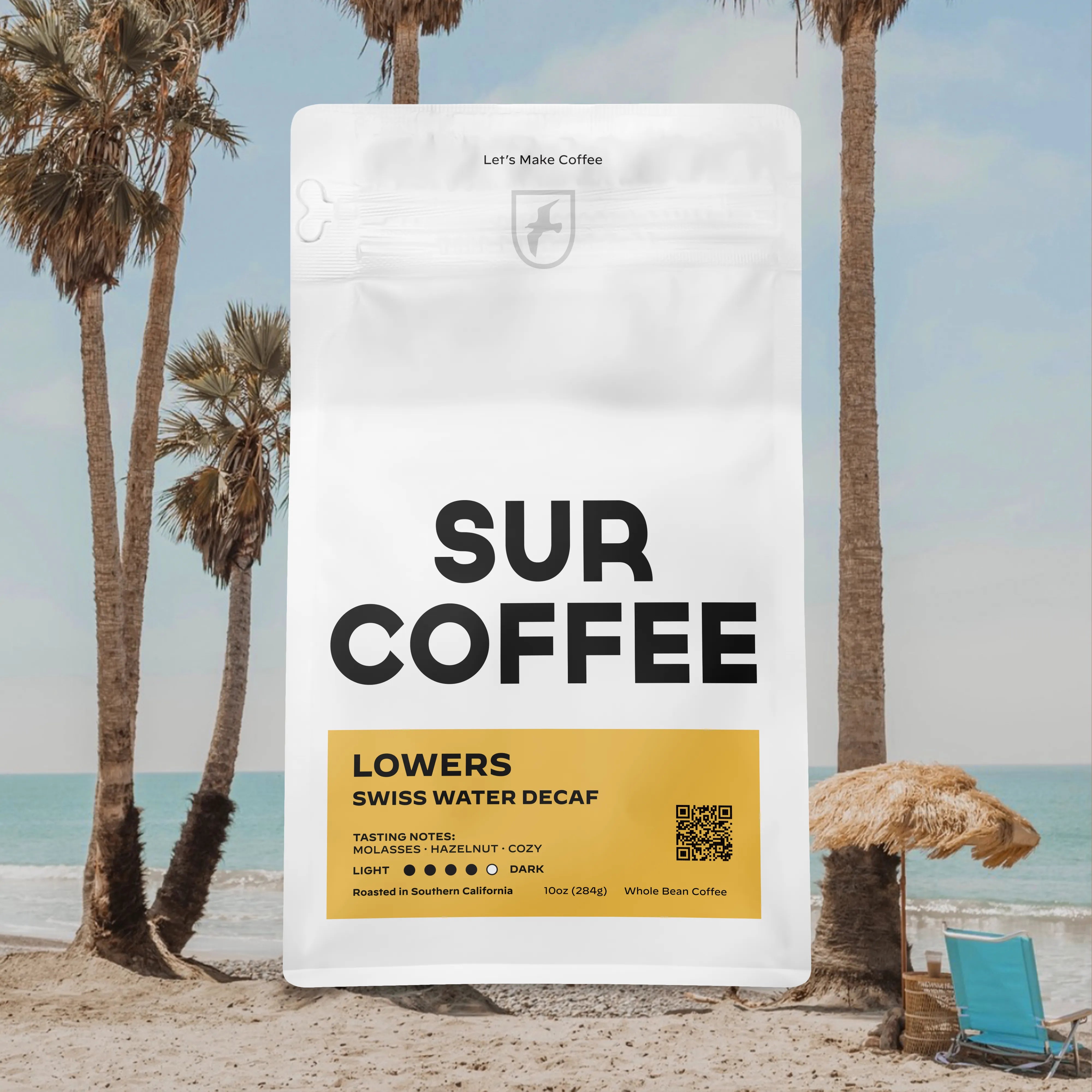 White bag of Sur Coffee Lowers Swiss Water Decaf with yellow label, palm trees and beach background.