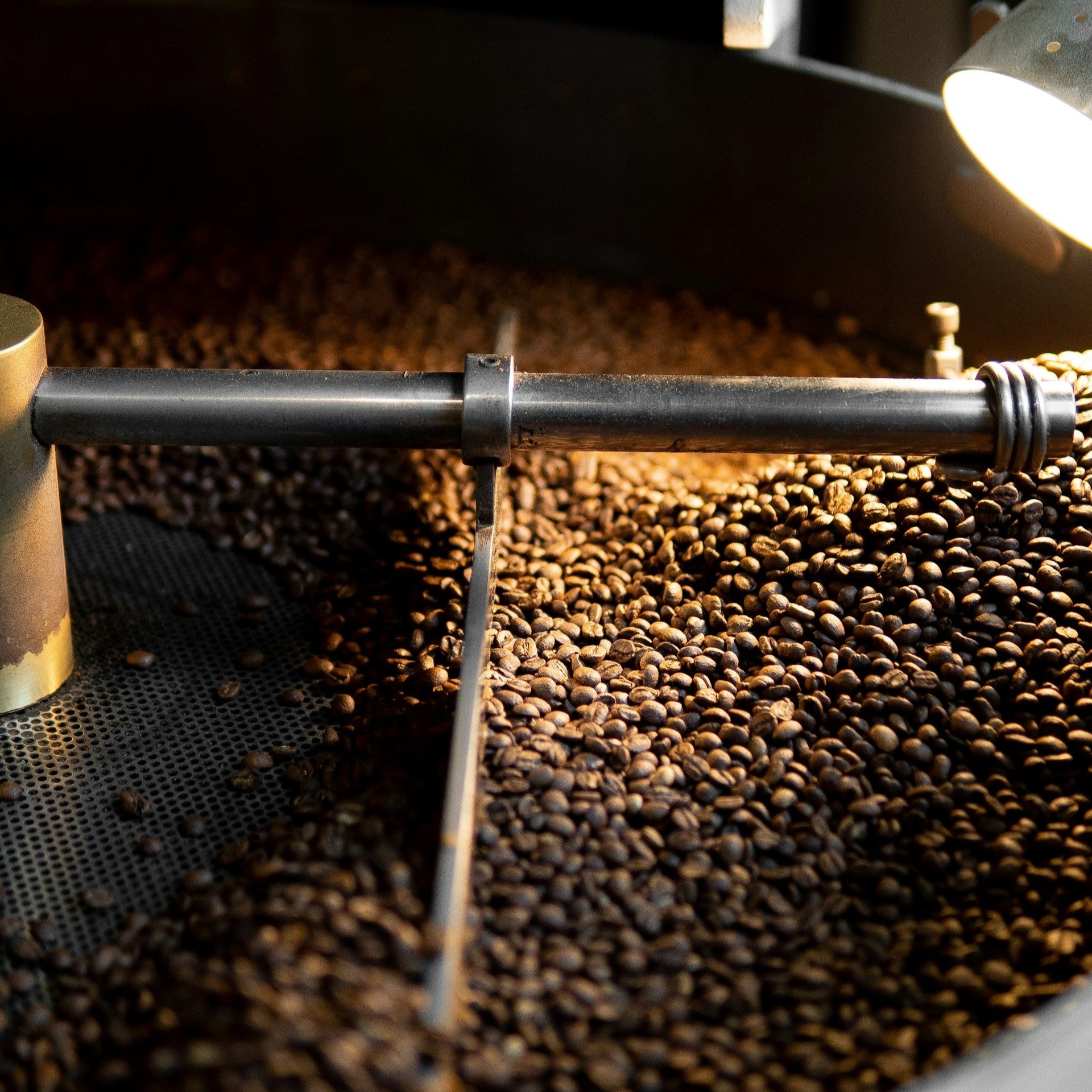 Close-up of dark roasted coffee beans inside a large industrial roaster with metal stirring arms.