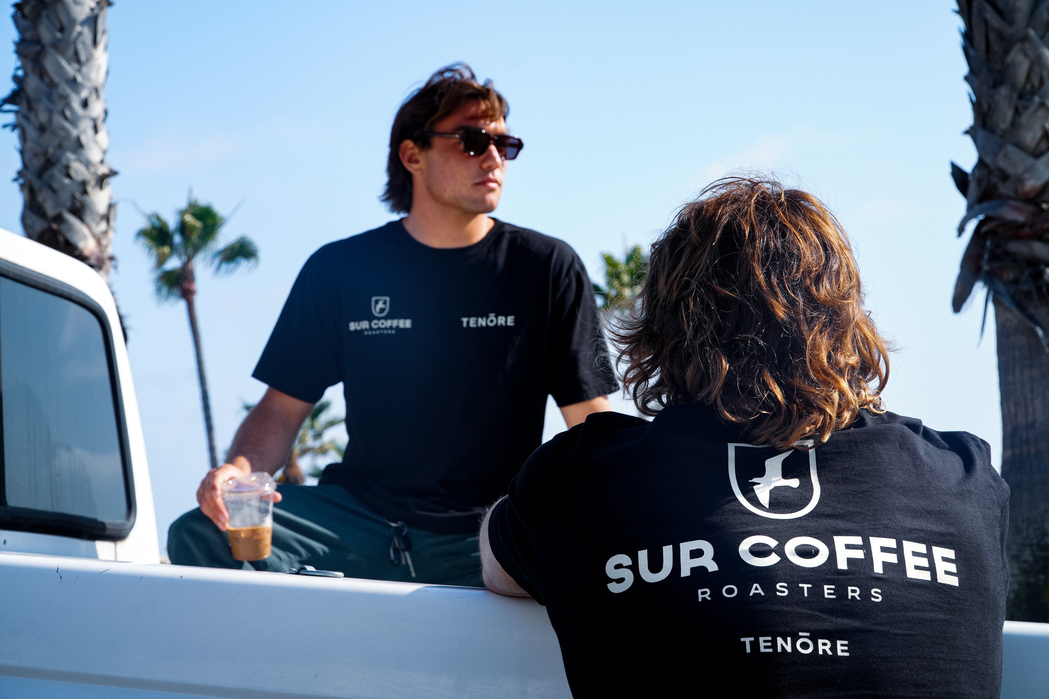 Black Sur Coffee x Tenore crewneck t-shirts with white logo text on chest and back worn outdoors.
