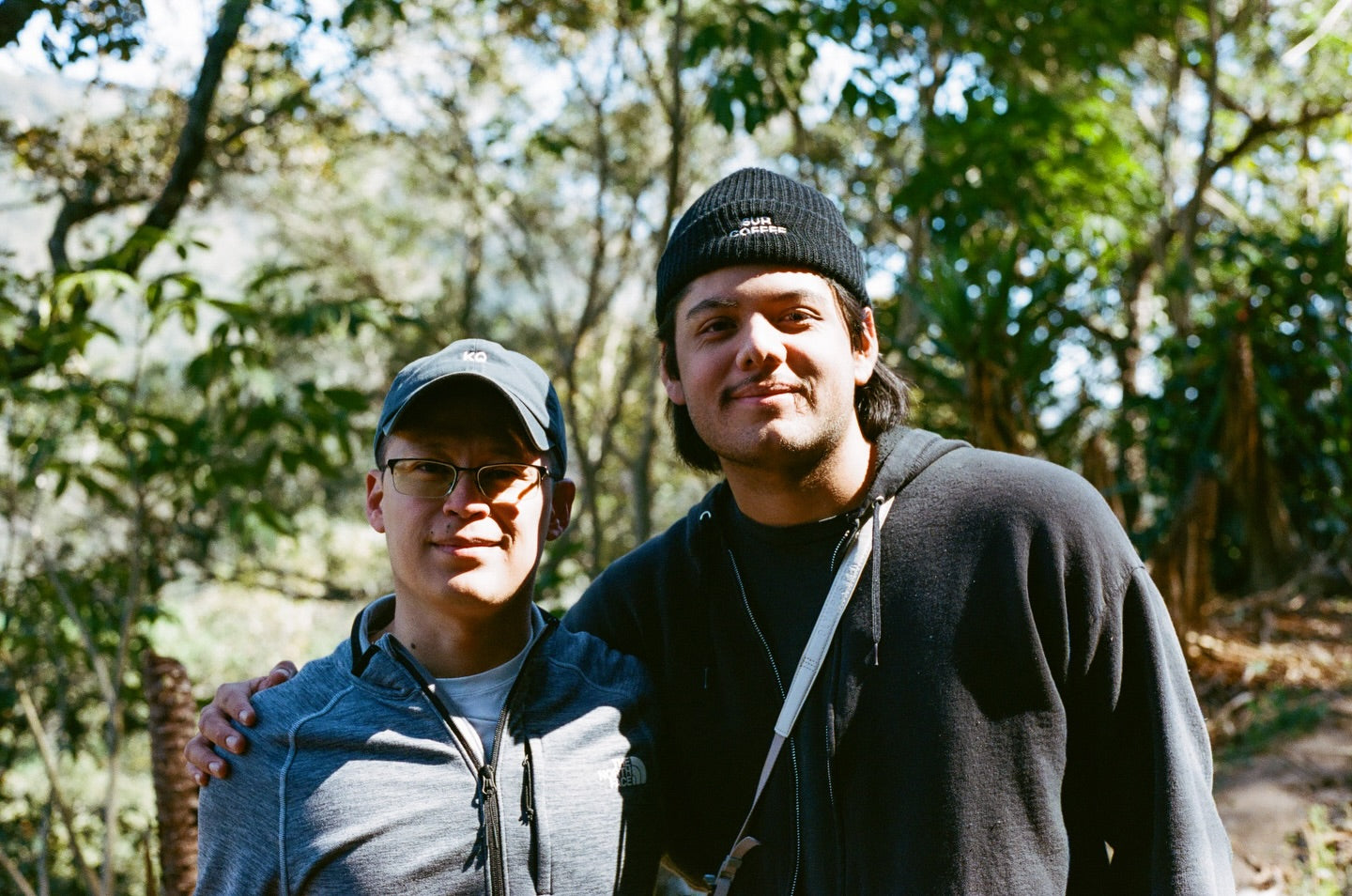 Two people standing outdoors with trees in the background